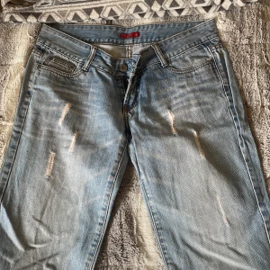 Blå jeans med slitningar - Snygga blå jeans från Redstar med slitningar på framsidan. De har en klassisk femficksdesign och knappgylf. Perfekta för en avslappnad stil.