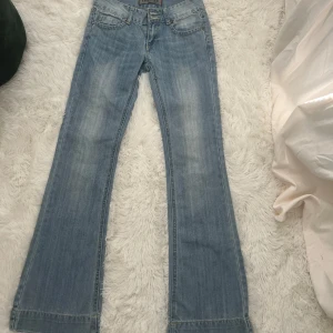 Ljusblåa lågmudjade bootcut jeans - Sjukt snygga lågmidjade ljusblåa bootcut jeans med söta detaljer!😍😍💗 Säljer då de tyvärr är försmå för mig. Midjemåttet fram: 35 cm innerbenslängd: 81🥰