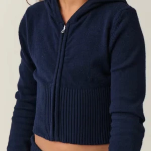 Mörkblå croppad hoodie - Säljer en mörkblå croppad hoodie med dragkedja och huva. Tröjan har långa ärmar och en ribbad nederdel som ger en snygg passform. Perfekt för en avslappnad stil. Passar som en s/m