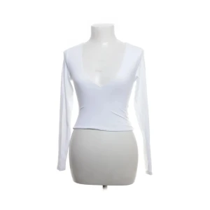 Vit långärmad topp från Babaton - Snygg vit långärmad topp från Babaton med djup v-ringning. Tillverkad i en mjuk och stretchig nylonblandning som ger en tight passform. Perfekt för en stilren look.