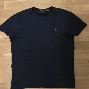 Mörkblå t-shirt från Ralph Lauren - Säljer en stilren mörkblå t-shirt från Ralph Lauren med det klassiska broderade logotypen på bröstet. T-shirten har en slim fit passform och är tillverkad i mjukt material för en bekväm känsla. Säljer pga fel storlek nu pris 1200