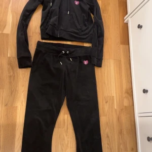 Svart velour hoodie och byxor från Juicy Couture - Säljer  svart velour hoodie och byxor  från Juicy Couture med dragkedja och huva. Den har ett glittrigt hjärta på bröstet och Juicy Couture-logga på ryggen och rumpan!