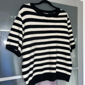 Svartvit randig stickad t-shirt från H&M - Säljer en svartvit randig tröja från H&M. Tröjan har en avslappnad passform med korta ärmar och är perfekt för en stilren look. Den är tillverkad i ett mjukt material som ger en bekväm känsla.