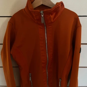 Orange jacka från Equestrian Stockholm - Snygg orange jacka från Equestrian Stockholm med dragkedja framtill och på fickorna. Storlek XS passar även sån som har XS/S. Frakt ingår ej i priset! Säljs ej längre på hemsidan. Pris: 255kr. Inga defekter så, väl omhändertagen. Kommer ej till användning längre. Färgen är Brick orange om jag minns rätt! 
