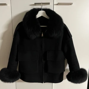 fur stockholm jacka med pälsdetaljer - Snygg svart jacka med pälsdetaljer på krage och ärmslut. Jackan har dragkedja framtill och stora fickor. Perfekt för kyliga dagar.