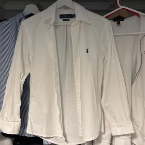 Vit skjorta från Ralph Lauren - Säljer en klassisk vit skjorta från Ralph Lauren med långärmad design och broderad logotyp på bröstet. Skjortan har en stilren look med knappar framtill och är perfekt för en elegant stil.