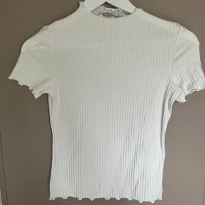 Vit ribbad topp från ONLY - Säljer en stilren vit ribbad topp från ONLY. Den har en tight passform och korta ärmar, perfekt för en enkel och snygg look. Toppen är tillverkad i ett mjukt material som känns skönt mot huden.