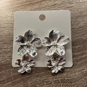 Silvriga blommiga örhängen - Snygga silvriga örhängen i form av blommor. Perfekta för att ge en elegant touch till din outfit. De har en vacker glans och är lätta att matcha med olika stilar.
