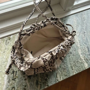 Ormmönstrad axelväska - Snygg axelväska med ormmönster i beige och svart. Väskan har en praktisk dragskoöppning och långa axelband. 