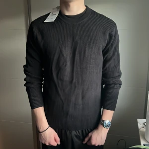 Svart stickad tröja från Zara - Säljer en stilren svart stickad  tröja från Zara. Perfekt för en minimalistisk look med långa ärmar och rund hals. Passar bra till allt. Tröjan är aldrig använd och därför i 10/10 skick. Nypris 430kr mitt pris 149kr.