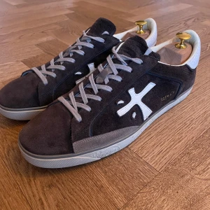 Bruna Premiata sneakers - Snygga bruna sneakers från Premiata i mocka med vita detaljer och grå snörning. Skorna har en rund tå och en diskret logga på sidan. Perfekta för en stilren look. Skorna är i otroligt bra skick! Allt originellt medföljer. Hör av er vid intresse så löser vi en smidig affär!🤩 