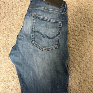 Blå jeans från Jack & Jones - Tjo, Snygga blå jeans från Jack & Jones W27-L30 med en sliten look och en liten reva på ena benet. Skick 8-10 använd några gånger. Pris kan diskuteras 