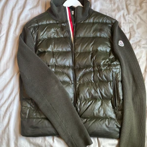 Grön Moncler cardigan Strl M - Säljer en fin grön cardigan perfekt till våren/sommaren. Jackan är äkta och kan scannas som på bilderna. Finns ett litet hål men det syns inte när man bär den eftersom det är innanför dragkedjan. Priset kan diskuteras!
