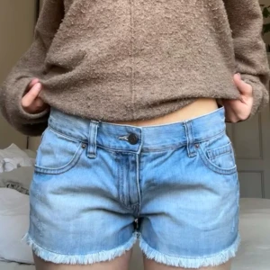 Lågmidjade jeansshorts med fransar - Snygga blå jeansshorts med fransiga kanter. Perfekta för sommardagar och avslappnade stunder. Klassisk femficksdesign och knappgylf.