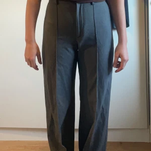 Grå kostymbyxor från Pull&Bear - Snygga grå kostymbyxor från Pull&Bear med hög midja och rak passform. Perfekta för en stilren look. Byxorna har en klassisk design med diskreta detaljer och är tillverkade i ett bekvämt material.