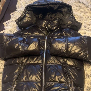 Svart  glansig pufferjacka med luva  - Snygg svart pufferjacka säljer då den inte kommer till användning längre har använts fåtal gånger och är i bra skick 💗