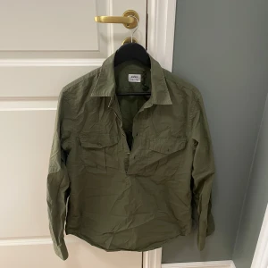 Aspesi overshirt - Säljer en stilren grön overshirt från Aspesi. Skjortan har långa ärmar och en klassisk krage. Perfekt för en avslappnad men ändå snygg look. Den har knappar framtill och två bröstfickor med lock.