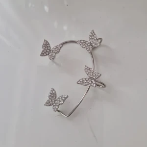 Silverfärgad öronaccessoar med fjärilar - Elegant silverfärgad accessoar dekorerat med glittrande fjärilar. Perfekt för att lägga till en touch av glamour till din outfit. Den har en öppen design som gör det enkelt att justera efter örat