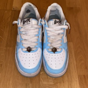 Blå och vita sneakers från Bape - Snygga Bape sneakers. Skorna har en klassisk design med stjärndetaljer på sidan och snörning framtill. Perfekta för att ge din outfit en cool touch.