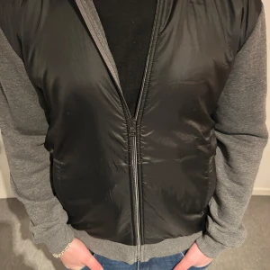 Svart och grå jacka från Hugo Boss - Snygg jacka från Hugo Boss med svart framsida och grå ärmar. Jackan är knappast använd och är i storlek L men passar M.