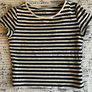 Randig kortärmad topp från H&M - Säljer en klassisk svartvit randig topp från H&M. Den har korta ärmar och en rund halsringning. Toppen är gjord i ett mjukt och bekvämt material men är lite liten i storleken. Kontakta för mer info! 