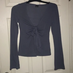  långärmad topp från Gina - Snygg topp från Gina med långa ärmar och en v-ringad design. Den har en knytning framtill som ger en fin detalj. Perfekt för både vardag och fest! 
