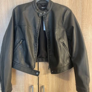 Mörkgrön  skinnjacka från Gina tricot  - Snygg mörkgrön  skinnjacka från Gina tricot  med dragkedja och knappar vid kragen. Jackan har en croppad passform och två fickor med dragkedja framtill. Perfekt för en cool look! Nytt pris :699:-