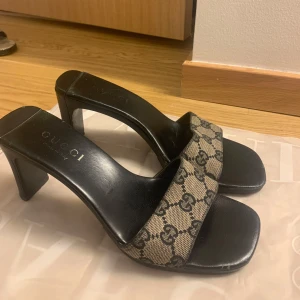Mönstrade klackskor från Gucci - Snygga klackskor från Gucci med ett ikoniskt mönster i beige och svart. Skorna har en öppen tå och en bred rem över foten. Perfekta för att ge en lyxig touch till din outfit. Köpta begagna. 8 cm klack.  Pris går att diskutera vid snabb affär. 