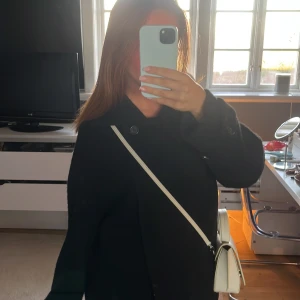 Svart kappa från Arket - Säljer en stilren svart kappa från Arket. Den har en klassisk design med knappar och en elegant krage. Perfekt till lite kallare vårdagar eller till hösten och vintern. Nypris 2000