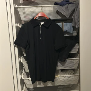 Svart pikétröja från Selected Homme - Säljer en stilren svart pikétröja från Selected Homme. Tröjan har en dragkedja framtill och korta ärmar, perfekt för en avslappnad look. Passar bra till både jeans och chinos. Storlek S men passar även M