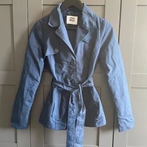 Mörkblå kort trenchcoat - En kort trenchcoat från Vero Moda i storlek XS. Jackan har knappar framtill och ett bälte i midjan, samt två fickor. Tunt material.