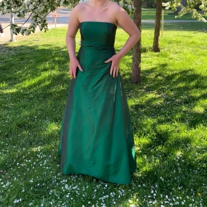 Grön axelbandslös långklänning - Säljer min gröna balklänning då den inte kommer till användning längre. Axelbandslös och smiter åt i midjan, tillkommer även en matchande scarf.