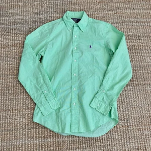 Grön Ralph Lauren Skjorta - Snygg grön skjorta från Polo Ralph Lauren i storlek S. Skjortan har långa ärmar och knappar framtill. Den är tillverkad i ett lätt och bekvämt material, perfekt för både vår och sommar. Den klassiska designen gör den lätt att matcha med olika outfits.