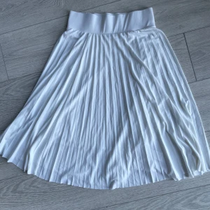 Vit plisserad kjol från Anna Field - Snygg vit plisserad kjol från Anna Field med elastisk midja för bekväm passform. Kjolen har en elegant och flödande design som passar perfekt för varma dagar. Tillverkad i ett lätt och luftigt material.