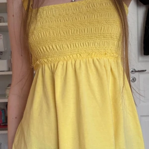 Gul babydoll top från Abercrombie & Fitch - Säljer en söt gul linnetopp från Abercrombie & Fitch. Toppen har breda axelband och en smockad överdel som ger en fin passform. Lite stygn som gått upp men inget som påverkar tröjan. Den har även en dekorativ spetskant längst ner. Perfekt för varma sommardagar!