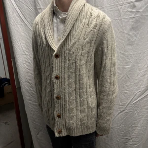 Beige stickad kofta från Hampton Republic L - Säljer en snygg beige stickad kofta från Hampton Republic. Koftan har ett klassiskt flätmönster och knäpps med träknappar. Den har en bred krage och långa ärmar. Passar både till vardags och mer uppklädda tillfällen. Plagget är i bra skick men lite nopprig. Plagget har storleken M men sitter som L. Modellen är 182cm/67kg