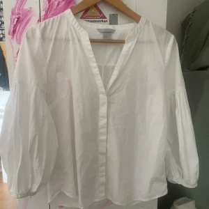 Vit blus med ballongärmar från H&M - Säljer en luftig vit blus från H&M med v-ringning och trekvarts ballongärmar. Blusen har en avslappnad passform och är tillverkad i bomull, perfekt för vår och sommar.
