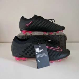 Nike Phantom Ultra Venom fotbollsskor svart/rosa - Säljer ett par Nike Phantom Ultra Venom fotbollsskor i svart med rosa detaljer och mönstrad ovansida. Skorna har snörning och en cool, skimrande yttersula. Perfekta för dig som vill sticka ut på planen!