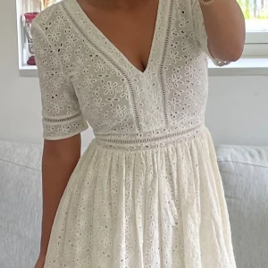 Vit broderad klänning med v-ringning - Superfin vit klänning med v-ringad hals och halvärmar. Klänningen har broderade blommor i spets och markerad midja. Perfekt för sommarens studentfiranden, endast använd en gång. Passar XXS-S