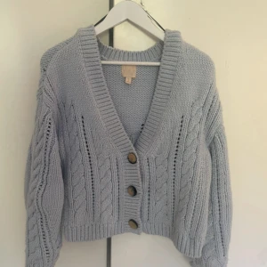 Stickad kofta - Superfin ljusblå stickad kofta med kabelstickat mönster och tre stora knappar framtill. Koftan är croppad och har långa ärmar samt bred ribbad kant vid ärmslut och nederkant🩵