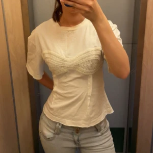 Vit t-shirt med virkad detalj - Säljer en vit t-shirt med unik virkad detalj över bysten . 
