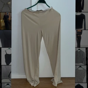 Beiga vida byxor - Säljer ett par beiga byxor med vid passform och hög midja. Byxorna har en enkel och stilren design utan synliga detaljer och är tillverkade i ett mjukt, lätt material som ger en skön känsla.