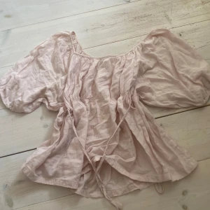 Ljusrosa blus från Lise Sandahl - Romantisk ljusrosa blus med vida ärmar och knytband i midjan. Blusen har en lös passform och är tillverkad i ett tunt, luftigt material som passar perfekt till varmare dagar.