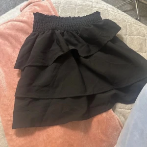 Svart volangkjol från H&M - Supersöt svart kjol från H&M med bred smock i midjan och dubbla volanger. Perfekt för dig som gillar en feminin och trendig stil. Kjolen är kort och har en flowy känsla. Storlek är 146/152 men passar mig som har mellan 32-26 eller XXS och XS och särkert S. Aldrig använd pga jag tycker den är lite kort. 