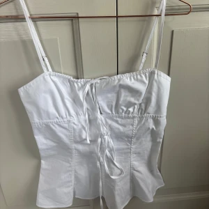 Vit linnetopp med knyt från Zara - Säljer en fräsch vit linnetopp från Zara med smala justerbara axelband och knytning framtill. Toppen har en enkel och stilren design, perfekt för varma dagar. Lappen sitter kvar.