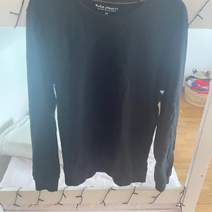 Svart långärmad tröja från Nudie Jeans - En stilren svart långärmad tröja från Nudie Jeans i ekologisk bomull. Tröjan har rund halsringning och är tillverkad av Fairtrade-certifierad bomull. Perfekt för en enkel och clean look.