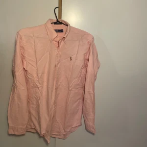 Ljusrosa skjorta från Polo Ralph Lauren - Säljer en klassisk ljusrosa skjorta från Polo Ralph Lauren med broderad logga på bröstet. Skjortan har knappar framtill och krage, perfekt för en stilren look. S-M 