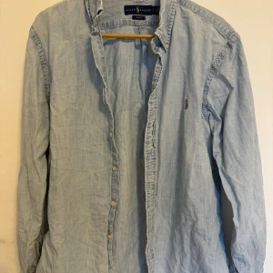 Ljusblå skjorta från Ralph Lauren - Skjortan är i denim/linnematerial och är i gott skick! Passar L såväl som M