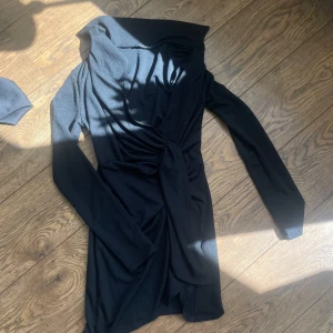 Svart omlottklänning med bälte - Säljer en svart omlottklänning med lång ärm och knytband i midjan. Klänningen har en snygg krage och är perfekt för dig som gillar stilrena plagg med en twist. Passar både till vardags och när du vill känna dig extra fin.