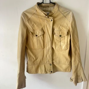 Beige skinnjacka - Snygg beige skinnjacka. Jackan har lång ärm och stängs med knappar och dragkedja. Ser lite mer gul ut i kameran än i verkligeheten🫶🏼